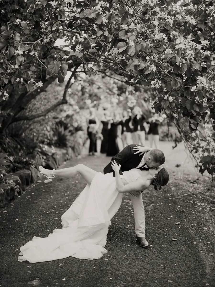 Groom dipping his bride for a kiss beneath a flowering tree in black and white
