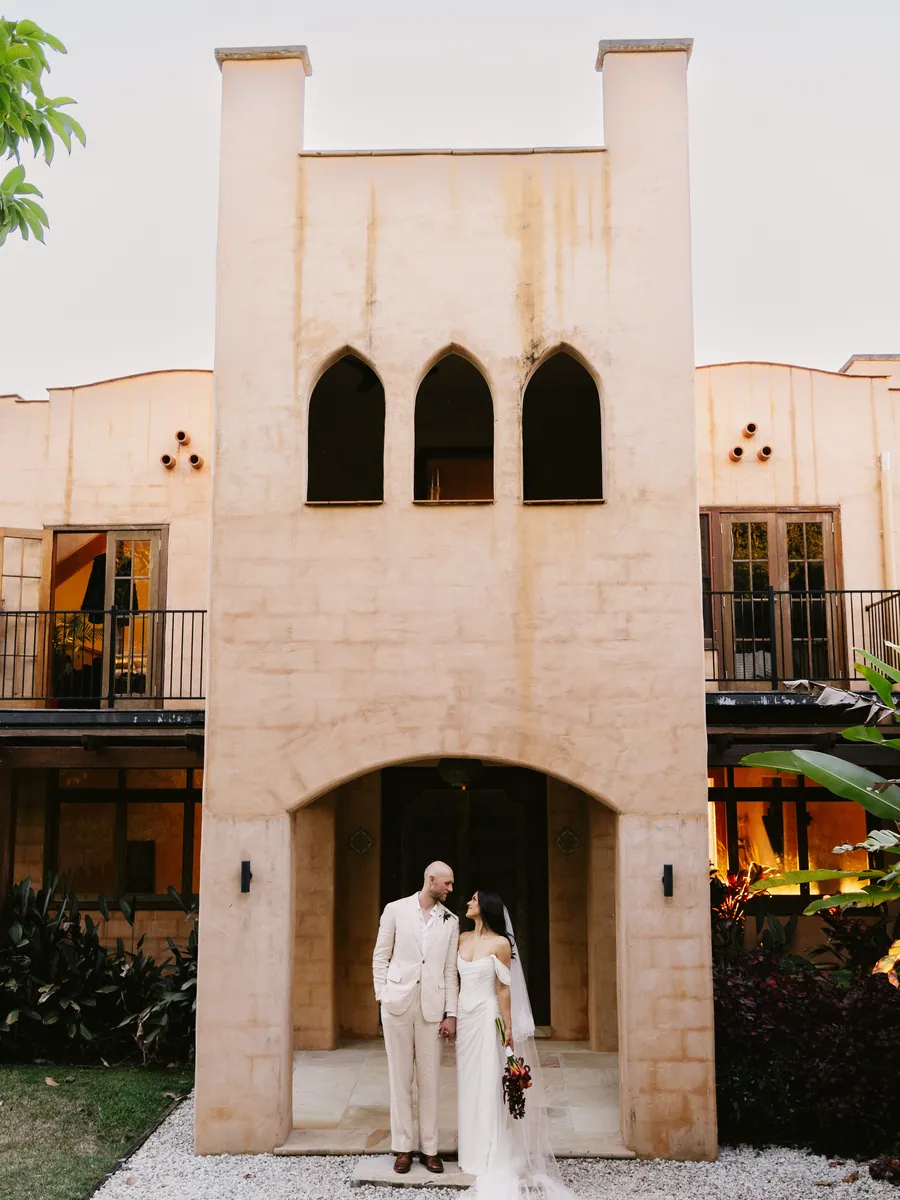Couple standing at the foot of a sunlit rendered villa tower