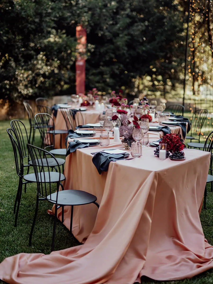 Blush satin tablecloth pooling on the lawn beneath a garden dinner table