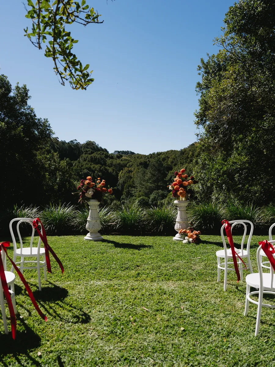 Garden ceremony aisle lined with white chairs and red ribbons