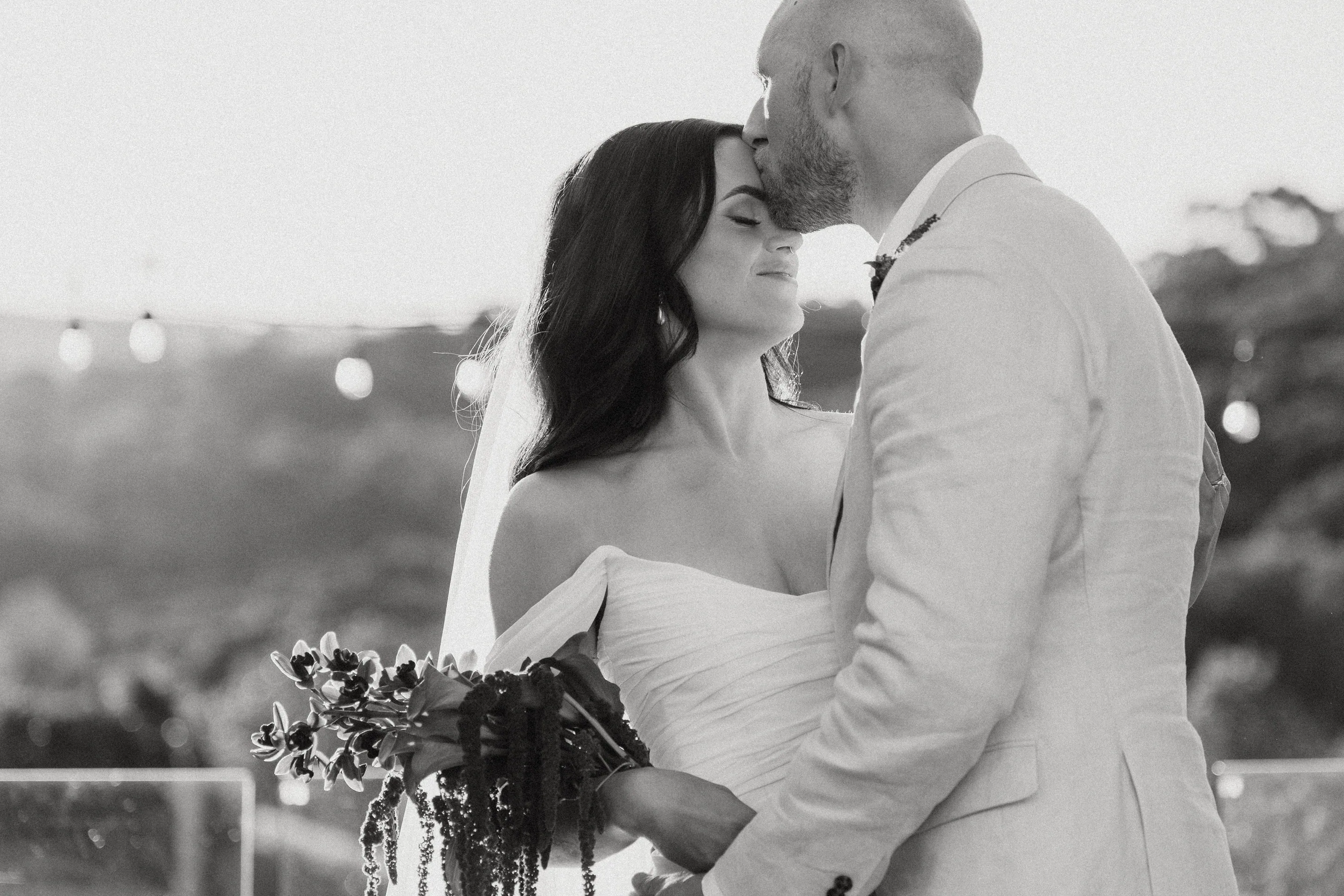Black and white image of a groom kissing the bride on the forehead