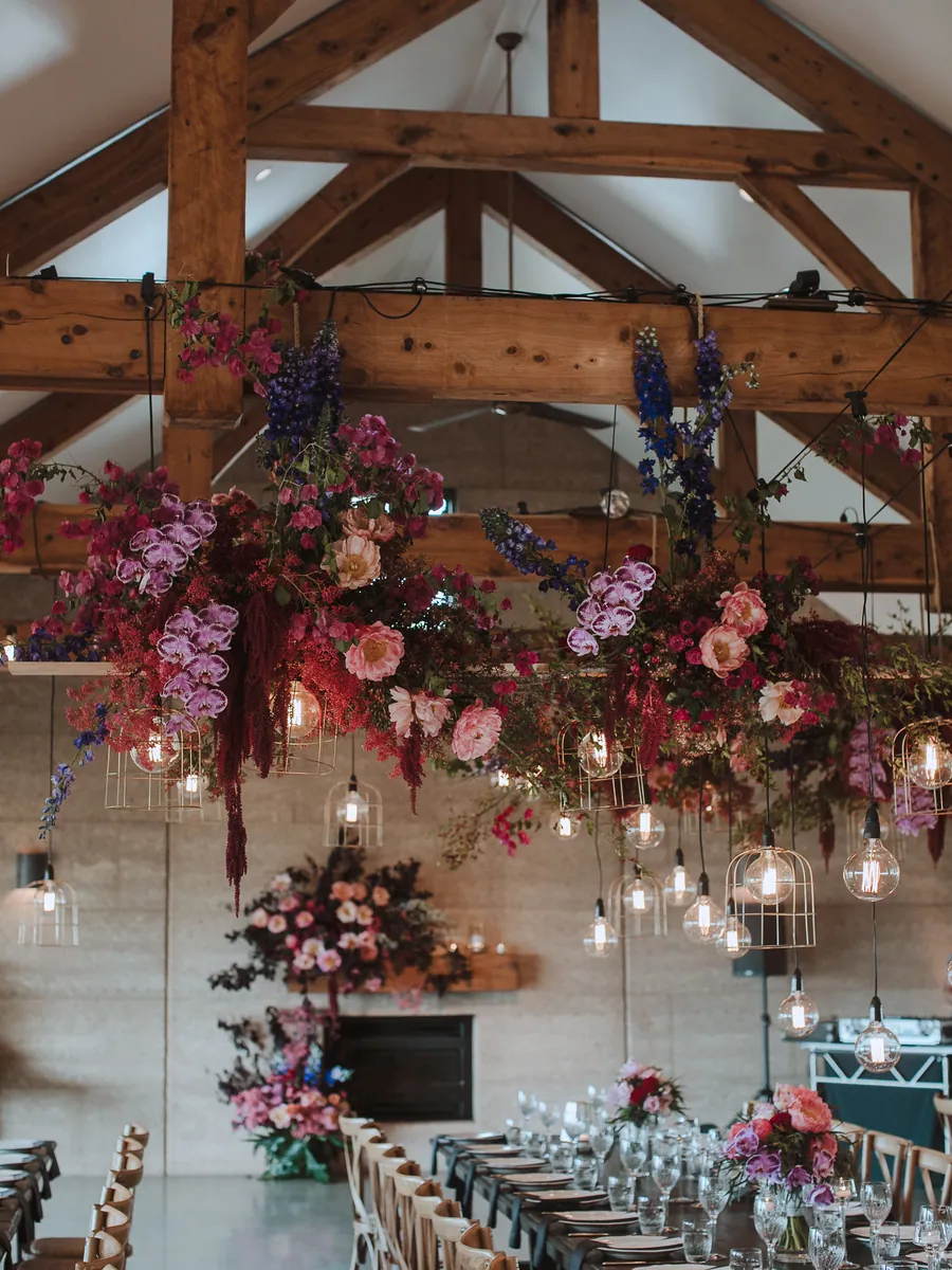 Floral installation suspended from timber trusses above a long reception table